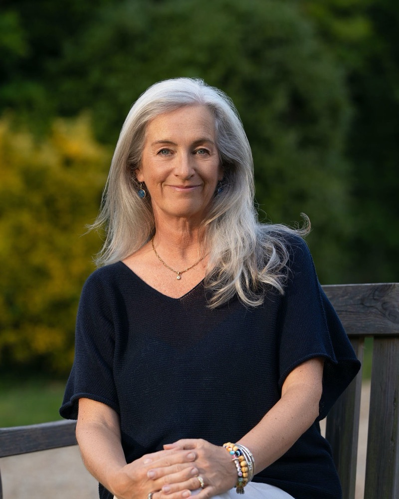 Jane Giles, smiling, sitting on a garden bench